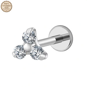 "Joia de piercing modelo labret prateado confeccionada em Titânio G23. Apresenta haste reta com base plana e topo decorativo com três pedras de zircônia redondas e brilhantes agrupadas em formato de triângulo. No canto superior esquerdo da imagem, há um selo atestando '100% Titânio G23 Biocompatível'. Ideal para perfurações em tragus, conch e helix."