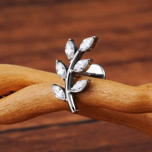 Piercing labret de titânio prata design ramo com 6 zircônias em formato de folhas sobre superfície de madeira