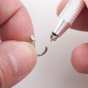 Pinça garra 4 pontas segurando pequena joia de piercing