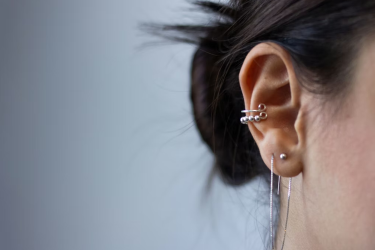 Imagem mostra uma orelha com piercings prateados muito bem colocados
