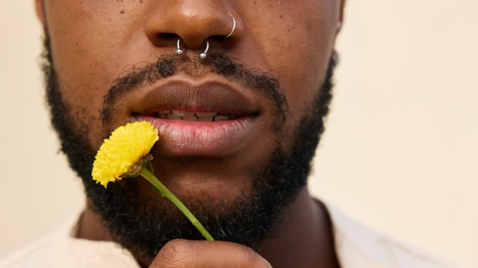 Homem com piercing no septo segurando flor amarela — exemplo de posicionamento correto do furo na região nasal