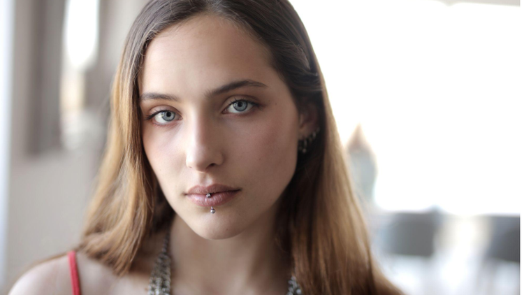 retrato frontal de uma mulher jovem com olhar sereno e cabelos castanhos claros e piercings.