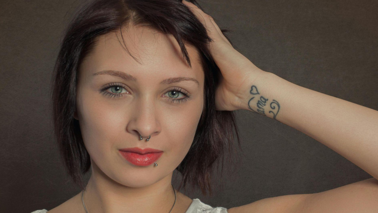 Ela usa um piercing de septo (argola no nariz) e um piercing de labret lateral (abaixo do lábio inferior).