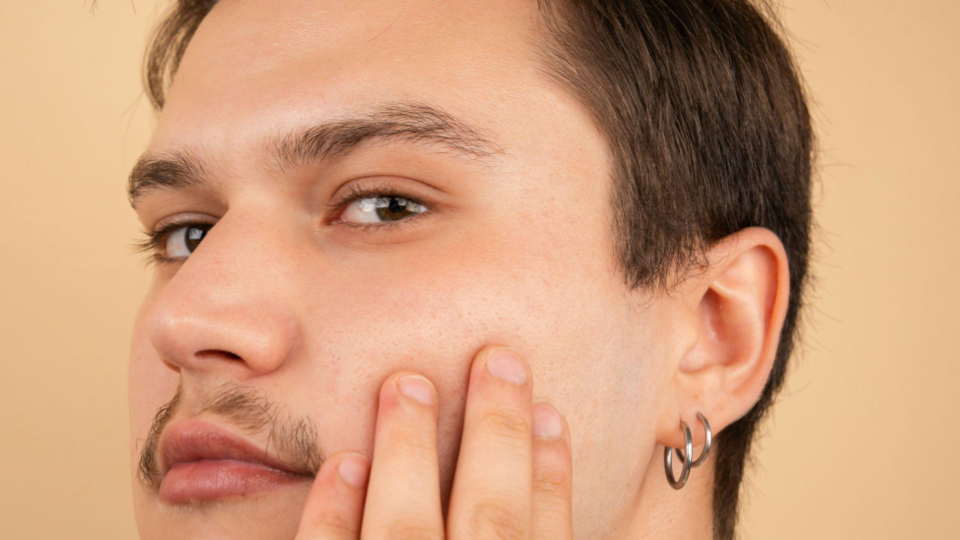 Imagem mostra o rosto de um homem e nas orelhas exibe piercings prateados.