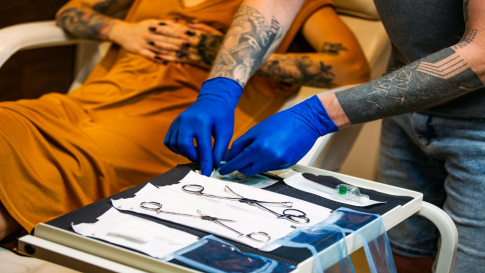 Cliente em um estúdio de piercing especializado, aguardando o especialista se preparar corretamente para o procedimento.