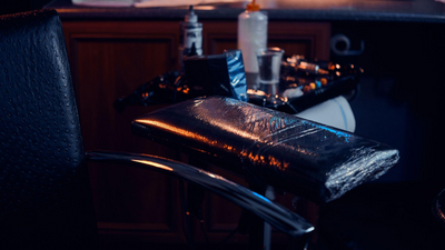 Fotografia com iluminação dramática de uma estação de trabalho de tatuagem. Em primeiro plano, um apoio de braço acolchoado revestido com plástico protetor descartável.