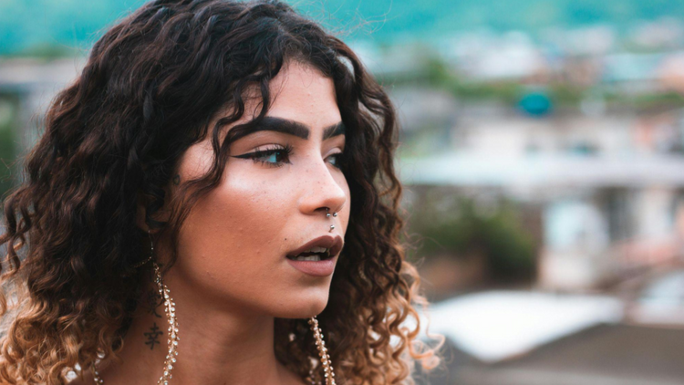 Uma mulher jovem com cabelos cacheados exibe vários piercings: um septo (argola com detalhe), um medusa (acima do lábio superior) e um vertical labret (atravessando o lábio inferior).