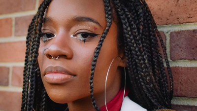 ela usa uma argola preta no nostril (aba lateral do nariz) e um piercing de ferradura (circular barbell) no septo.