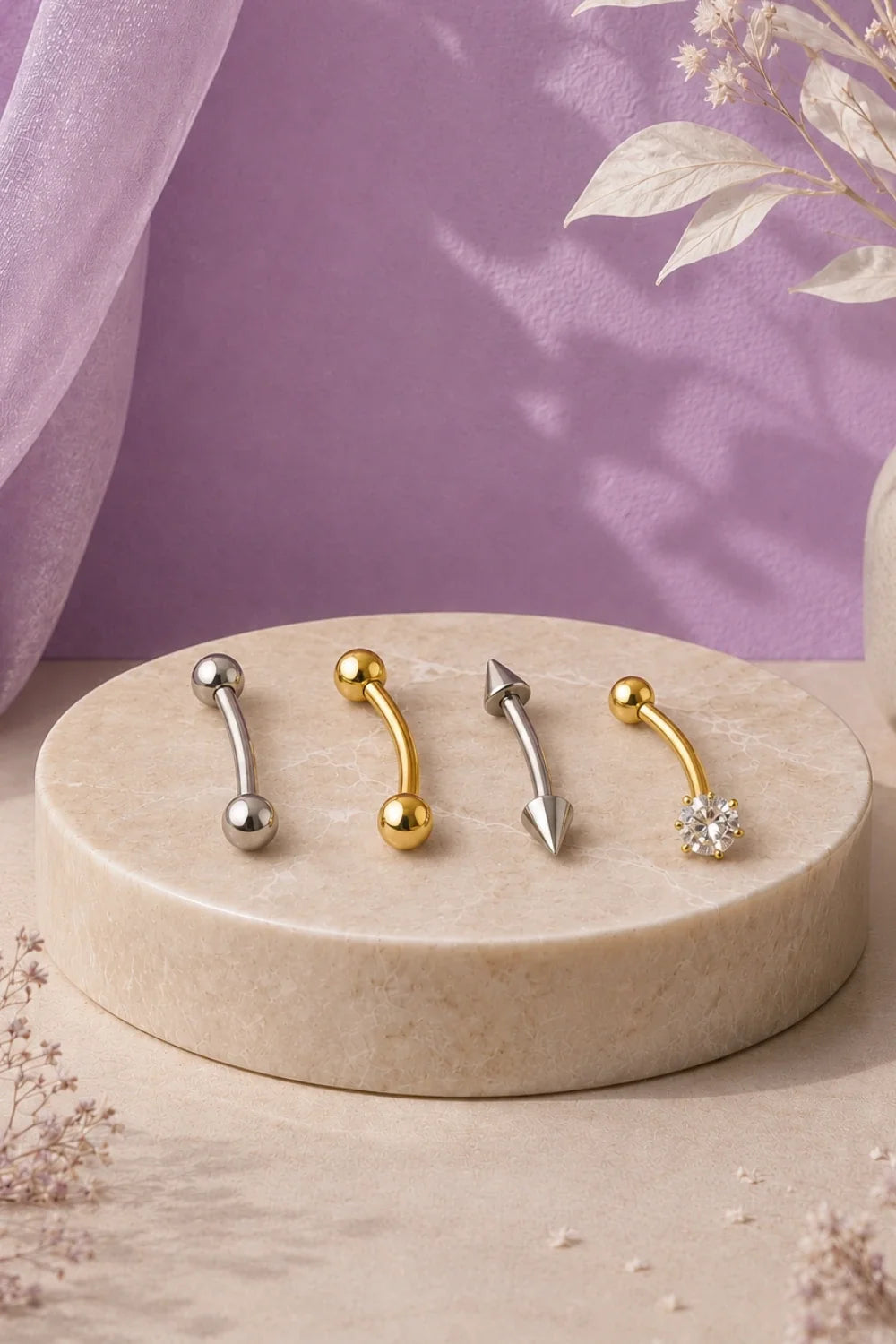 Dois piercings barbell prateado e dourado, nos modelos curvo e reto, sobre fundo marrom