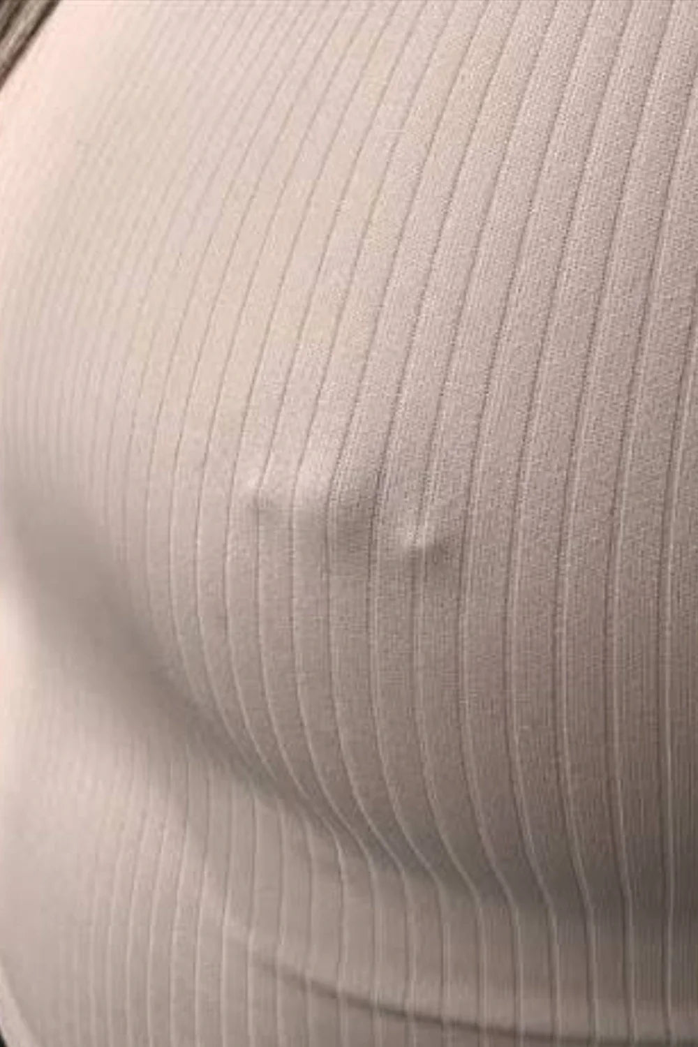 Blusa branca feminina com piercing mamilo modelo barbell aplicado abaixo do tecido.