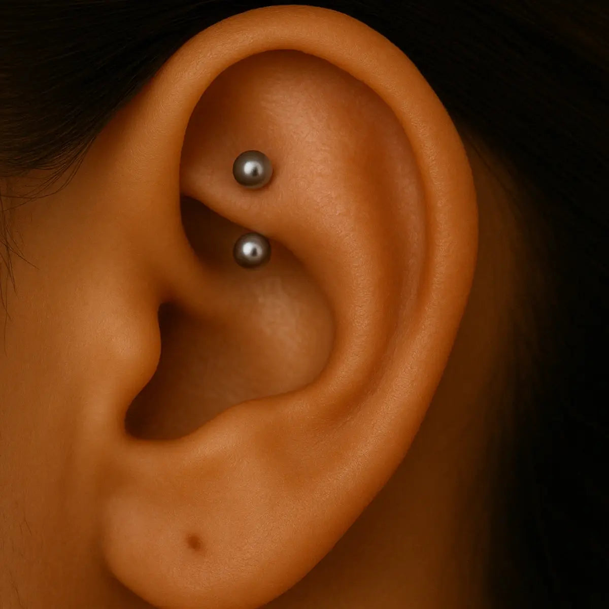 Piercing rook em titânio G23, barbell curvo com duas bolinhas metálicas prateadas, aplicado na cartilagem interna da orelha.