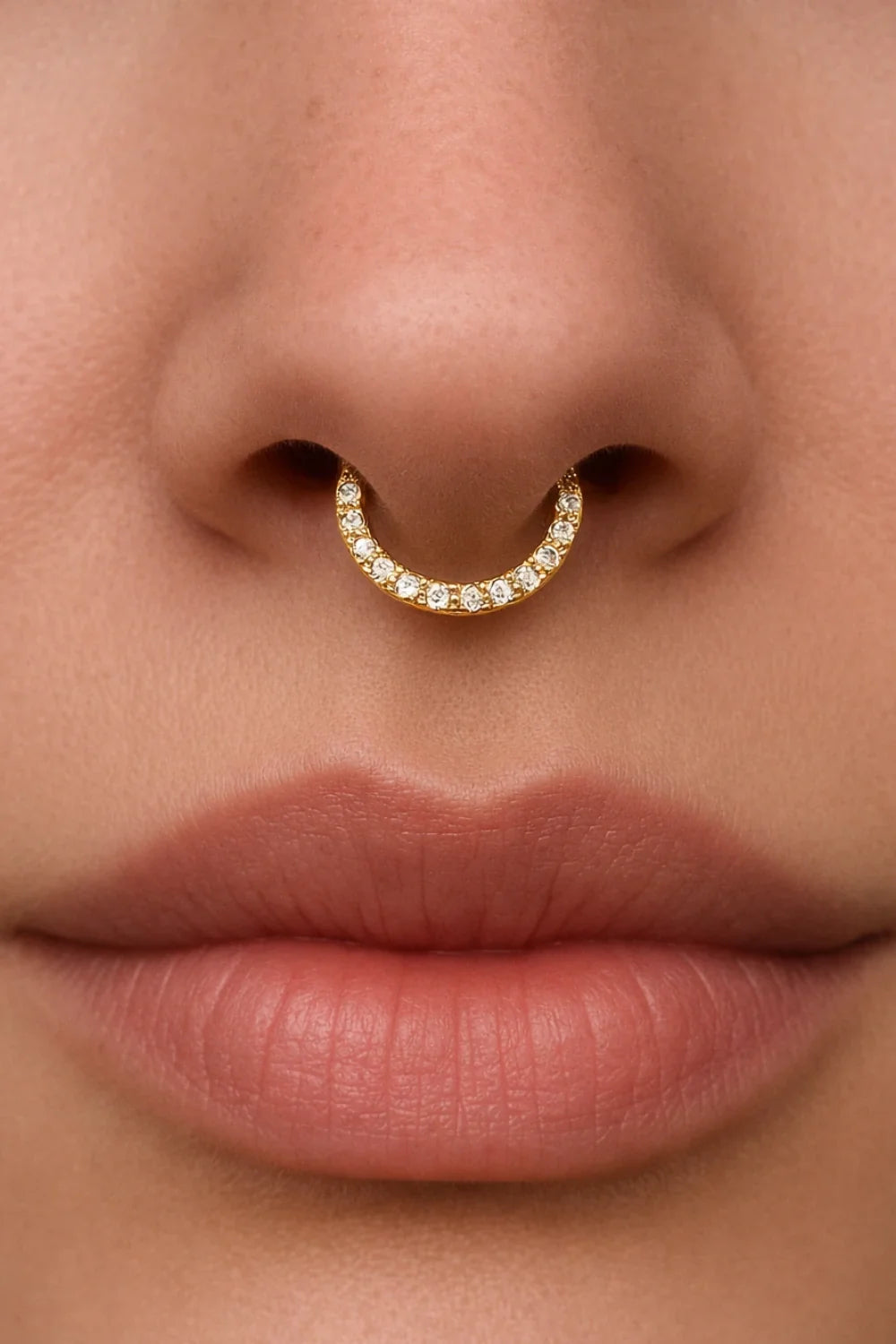 Piercing septo central no nariz, estilo argola dourada com pedras de zircônia na parte frontal.