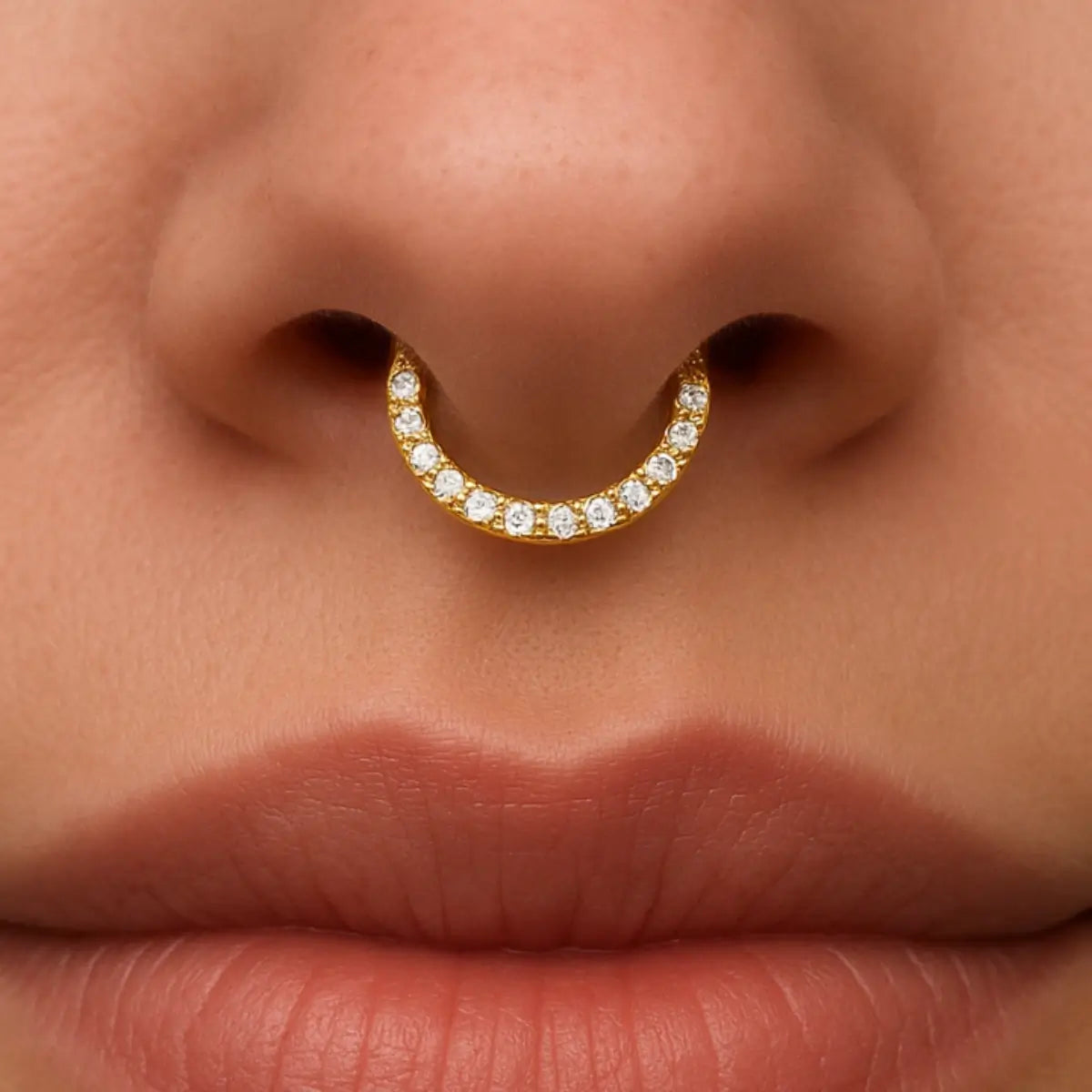 Piercing septo central no nariz, estilo argola dourada com pedras de zircônia na parte frontal.