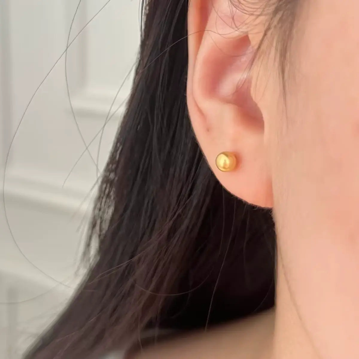 Brinco metálico de aço cirúrgico cor dourada formato bolinha em uso na orelha