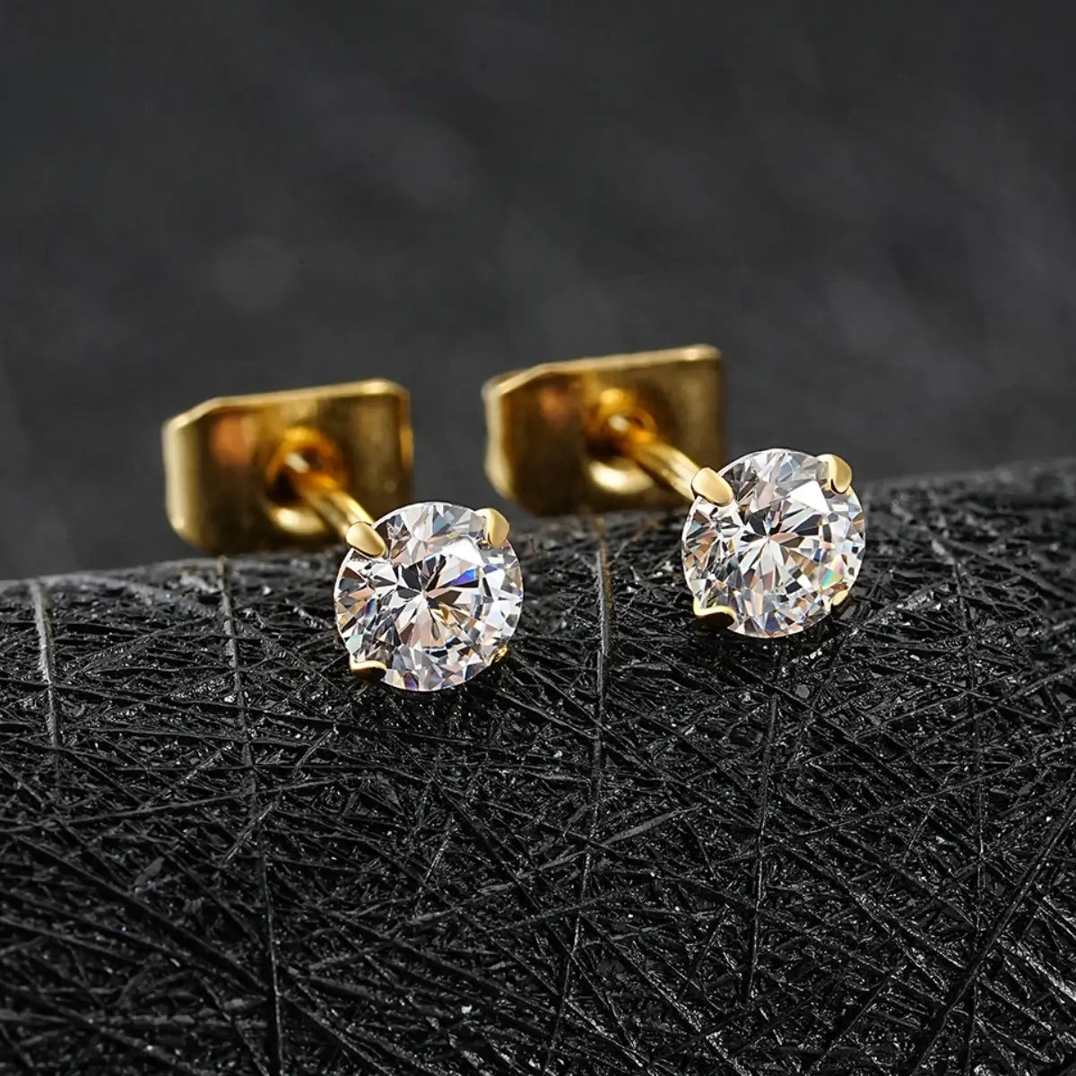 Brincos ponto de luz dourados com zircônias brilhantes sobre superfície texturizada preta em close