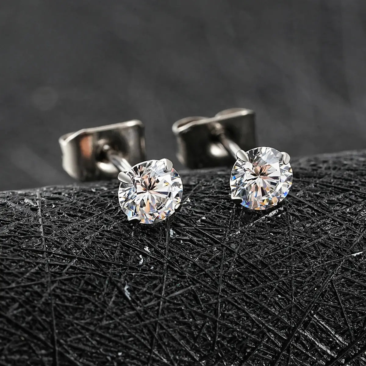 Brincos ponto de luz prateados com zircônias brilhantes sobre superfície texturizada preta em close