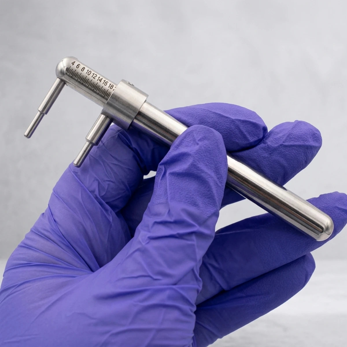 Body piercer segurando o piercímetro com luvas, demonstrando o uso profissional da ferramenta de medição