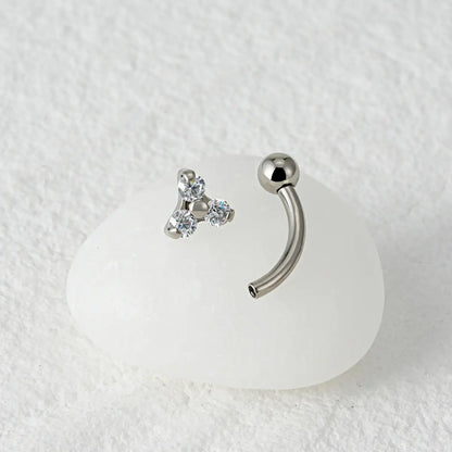 Piercing curvo banana prateado de titânio com 3 zircônias em detalhe sobre fundo de mármore