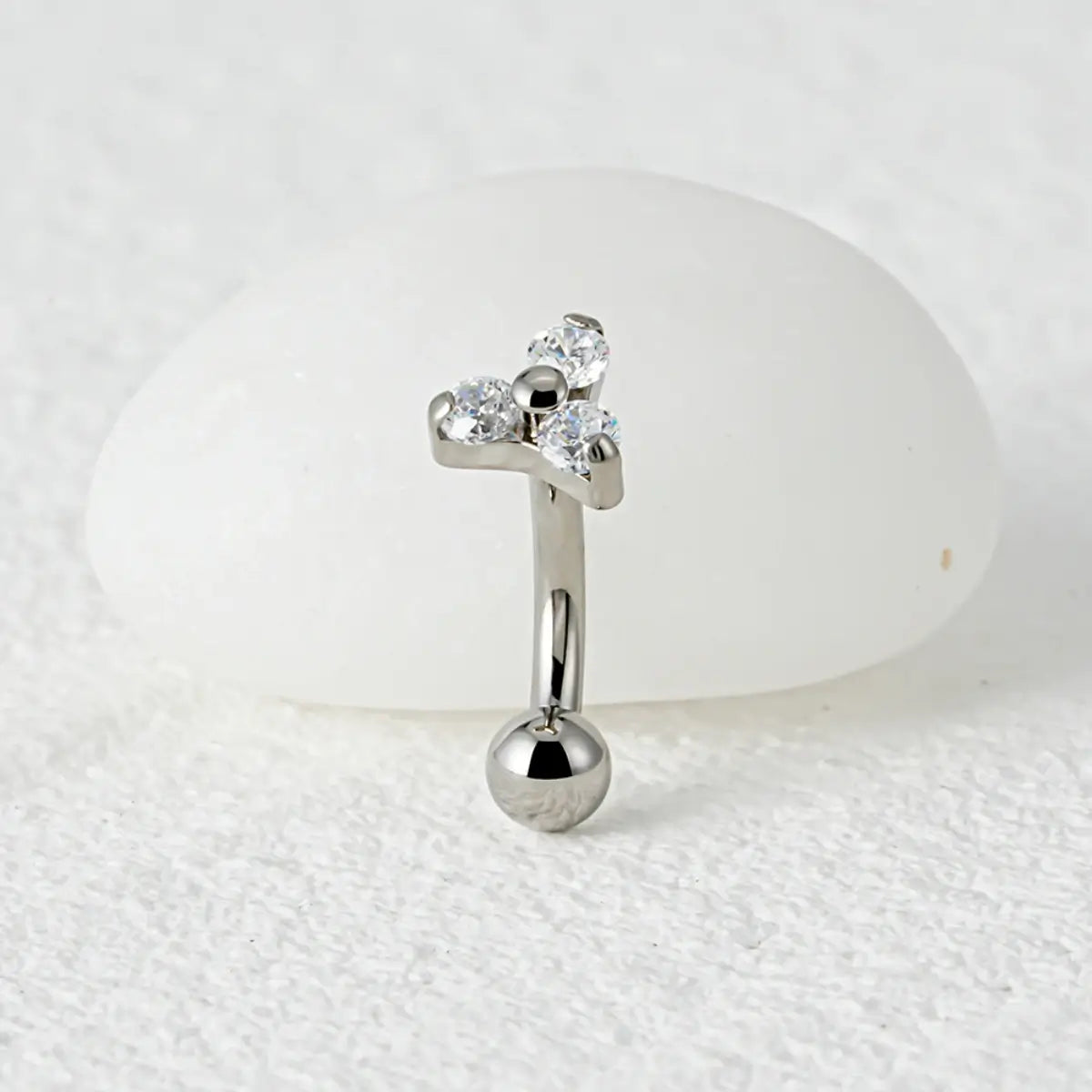 Piercing curvo banana prateado de titânio com detalhes das 3 zircônias cravadas sobre fundo claro