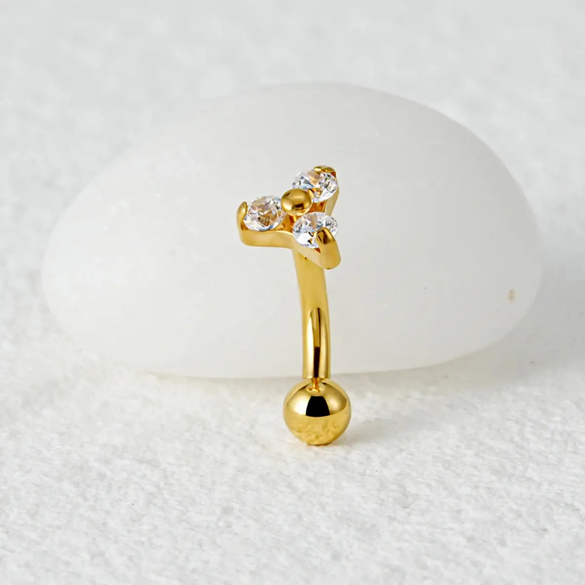 Piercing curvo banana dourado de titânio com 3 zircônias cravadas em detalhe sobre fundo claro