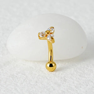 Piercing curvo banana dourado de titânio com 3 zircônias cravadas em detalhe sobre fundo claro