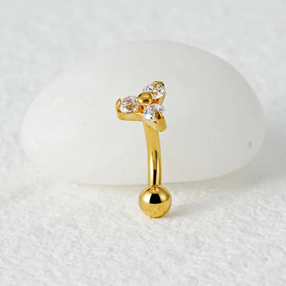 Piercing curvo banana dourado de titânio com 3 zircônias cravadas em detalhe sobre fundo claro