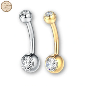 "Dois piercings curvos modelo banana bell feitos em Titânio G23, um na cor prateada e outro na cor dourada. Ambos possuem pedras de zircônia redondas e brilhantes cravadas nas esferas das extremidades. No canto superior esquerdo há o selo '100% Titânio G23 Biocompatível'. Joia ideal para umbigo, rook e sobrancelha."