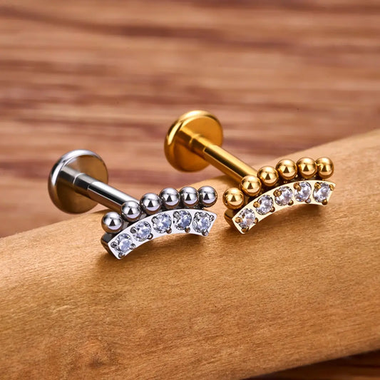 Piercing Labret de Titânio Cluster Curvo com Zircônia nas cores dourado e prata sobre madeira