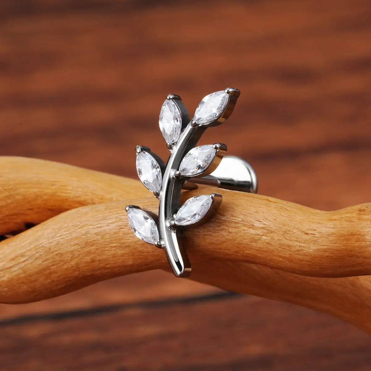Piercing labret de titânio prata design ramo com 6 zircônias em formato de folhas sobre superfície de madeira
