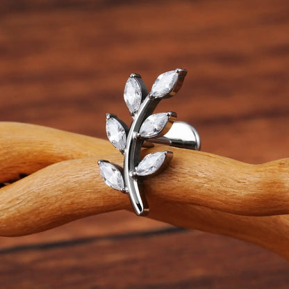 Piercing labret de titânio prata design ramo com 6 zircônias em formato de folhas sobre superfície de madeira