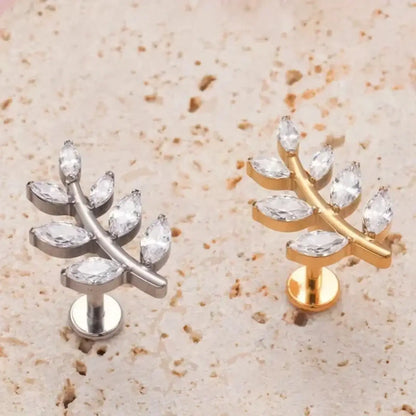 Piercings labret de titânio design ramo com 6 zircônias em formato de folhas nas cores prata e dourado sobre superfície clara