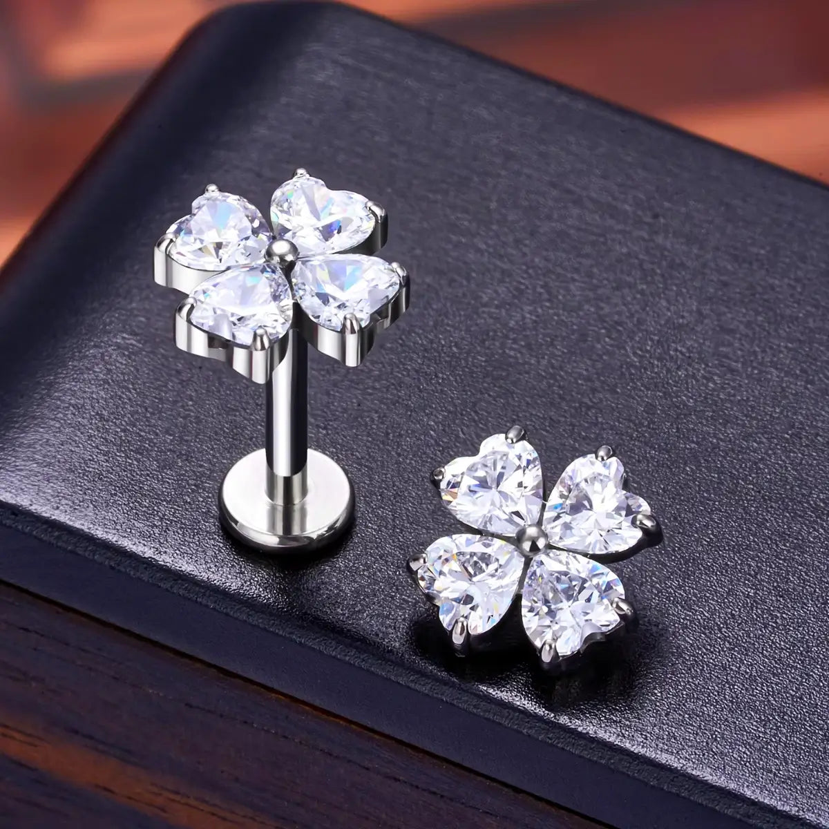 Piercings labret de titânio formato trevo prateado com zircônias sobre fundo escuro